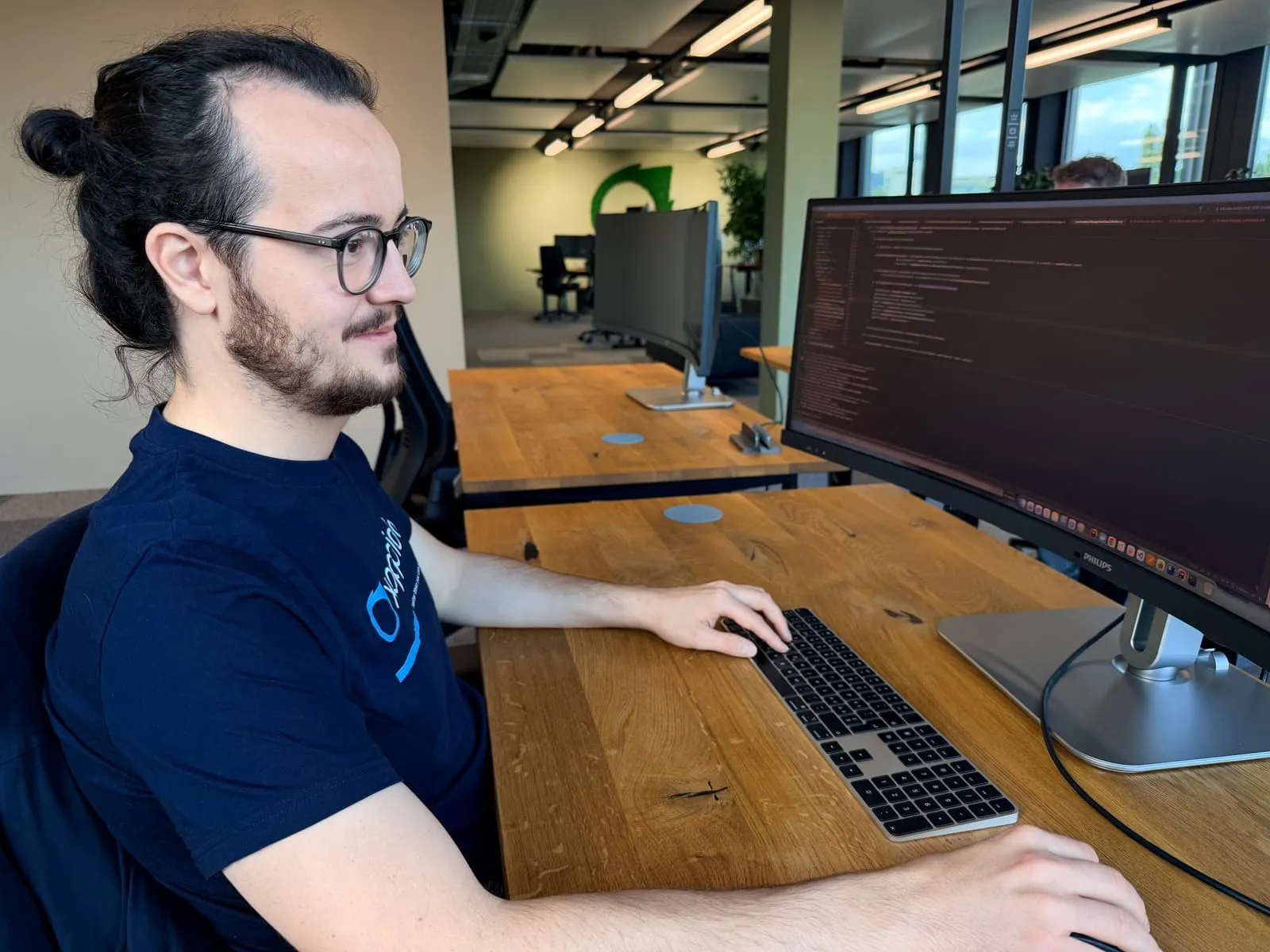 Pablo sitzt am Schreibtisch im Büro in Sursee und arbeitet an einem grossen Bildschirm mit Programmcode
