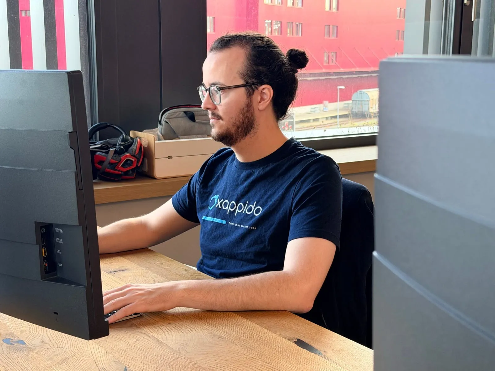 Pablo tippt konzentriert am Schreibtisch vor dem Fenster, hinter ihm ein rotes Fabrikgebäude