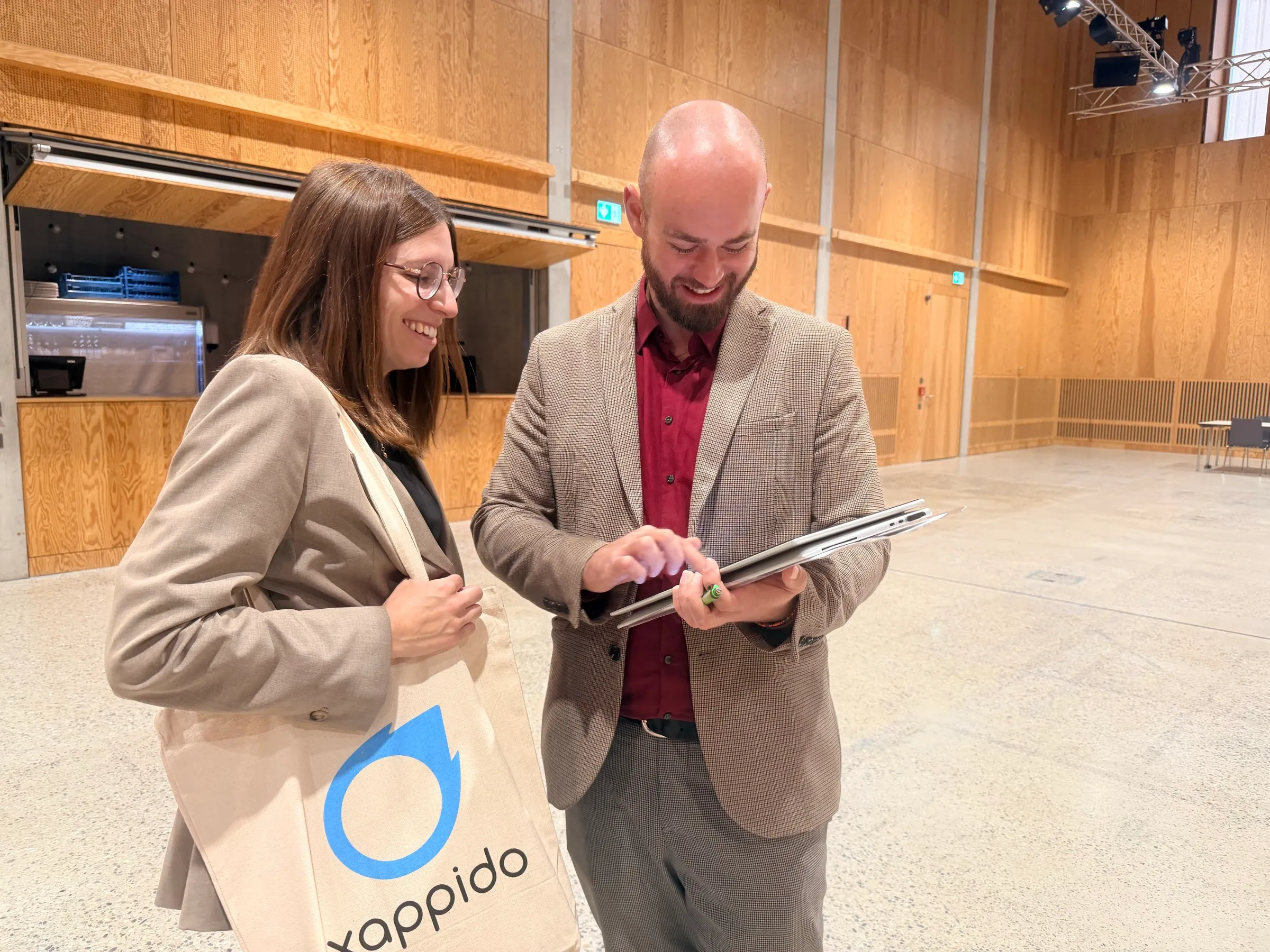Loredana von xappido und Zsolt Gödri vom CAMPUS SURSEE schauen gemeinsam auf die Einsatzplanung auf dem Tablet, im Hintergrund ein leerer Veranstaltungssaal