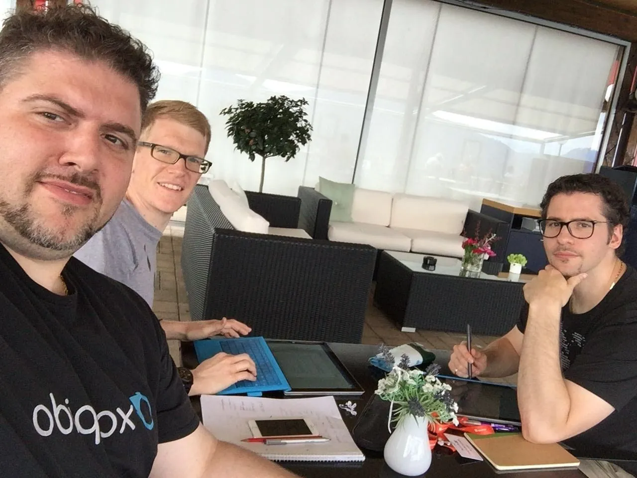 Arbeitssession zu dritt auf einer Terrasse, auf dem Tisch Tablet, Notizblock und Skizzen