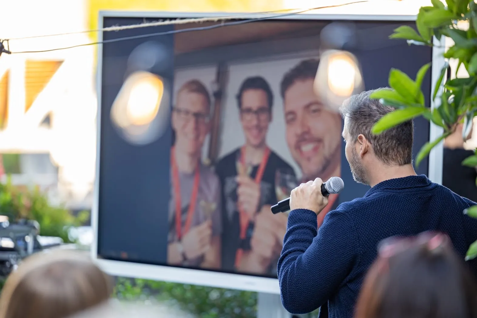 Begrüssung der Gäste, auf der Leinwand ein Bild des Gründertrios