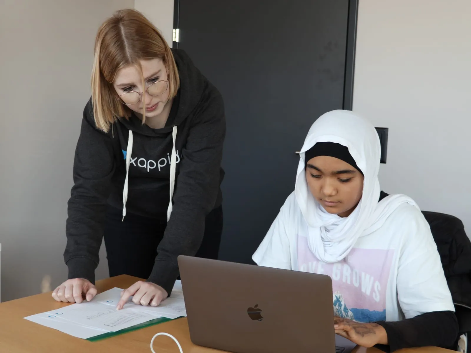 Eine Betreuerin zeigt auf das Arbeitsblatt, daneben eine Schülerin am Laptop