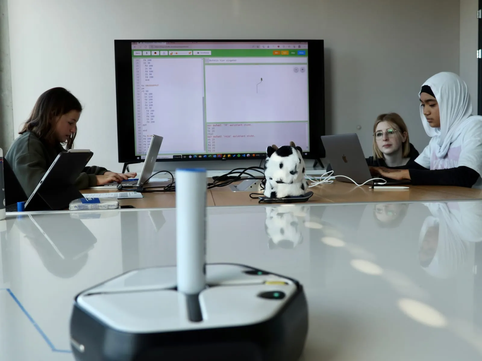 Lernroboter auf dem Tisch, dahinter der Bildschirm mit dem Programmcode