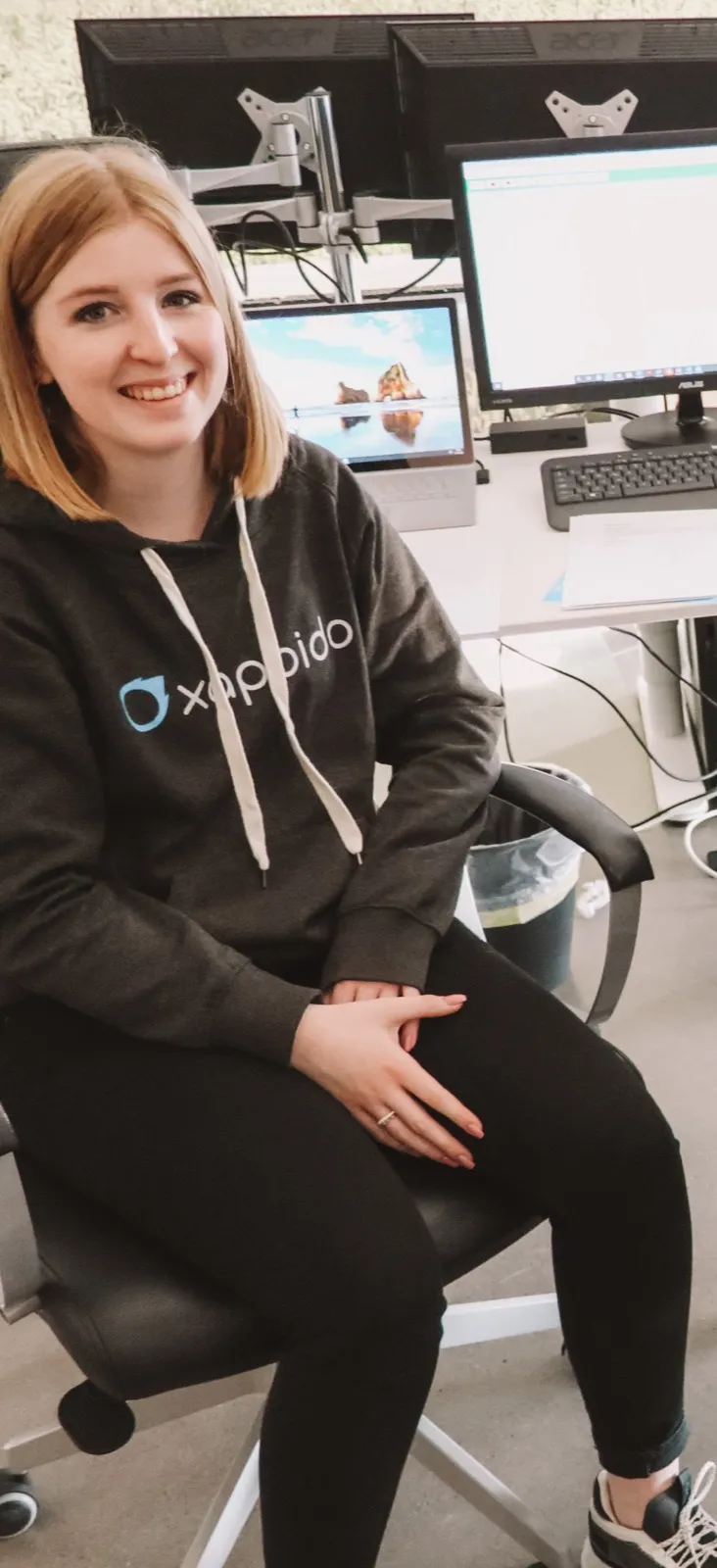 Lea an ihrem Arbeitsplatz im xappido-Hoodie, im Hintergrund ihre Bildschirme